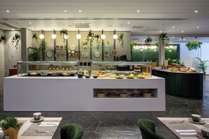 Een buffetgedeelte met diverse voedingsopties, een koffiehoek en hangende planten.