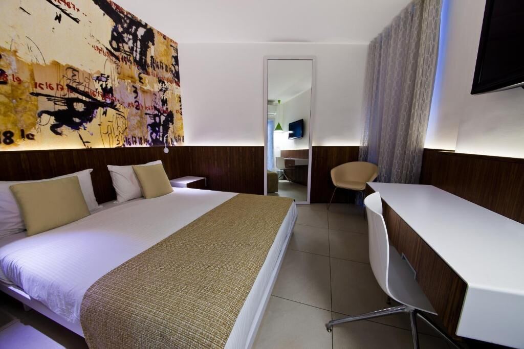 Habitación de hotel con una cama grande, un escritorio, una silla, un espejo y una pared con arte abstracto.