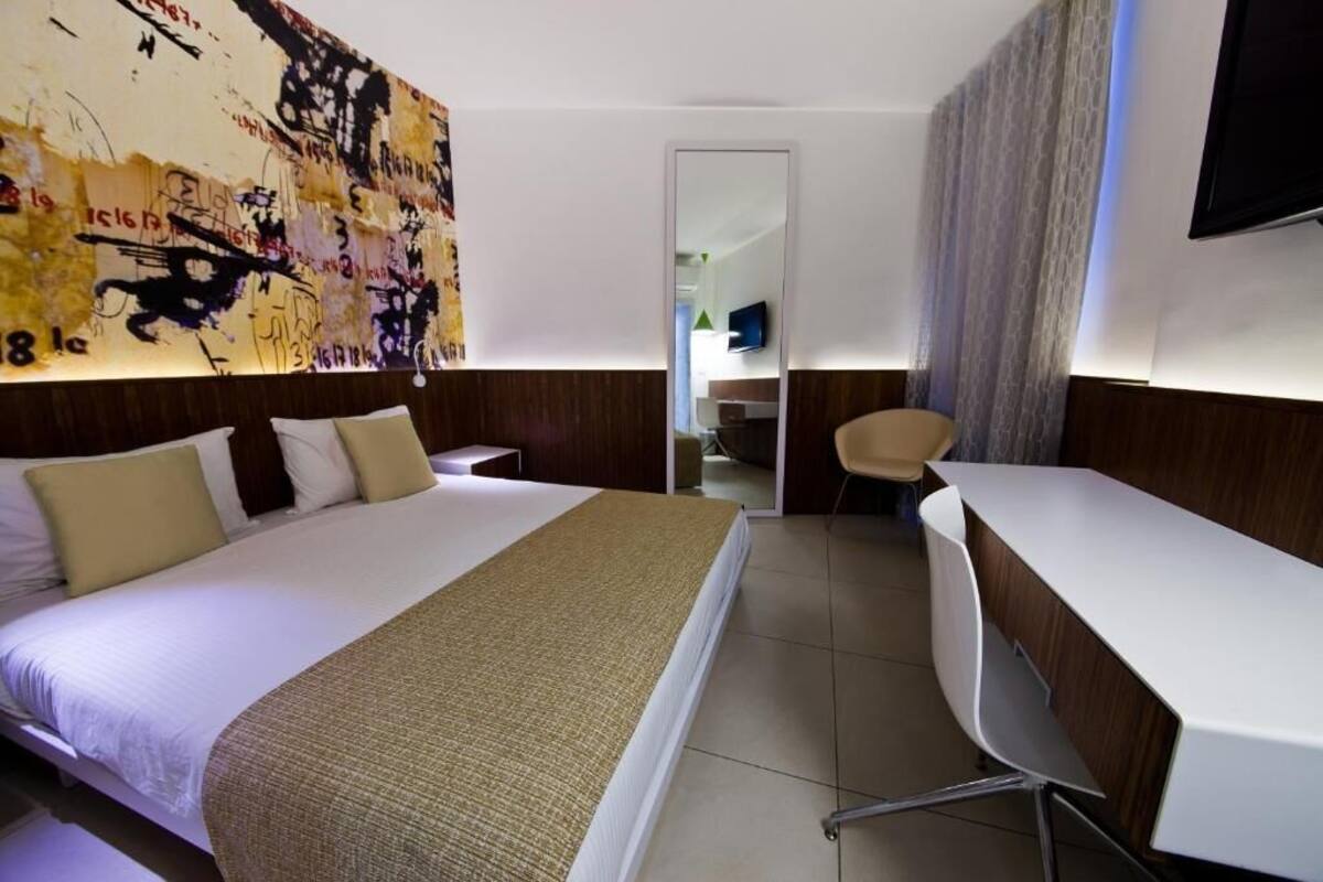 Habitación de hotel con una cama grande, un escritorio, una silla, un espejo y una pared con arte abstracto.