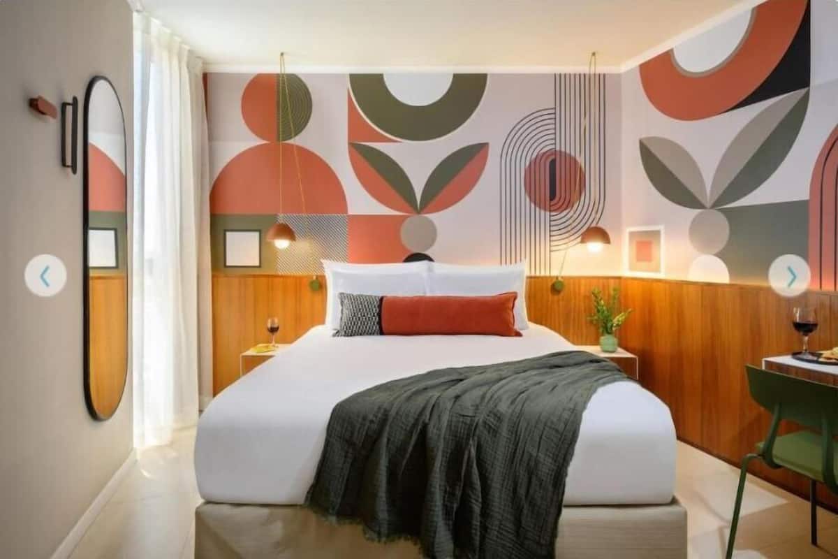 Un dormitorio moderno con una cama grande, una mesita de noche con lámpara, una silla verde y arte abstracto en la pared.