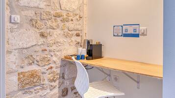 A small kitchenette with a stone wall, a wooden counter, a white chair, a coffee machine, and a kettle.