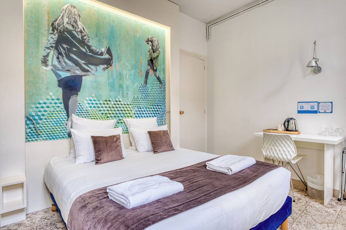 A hotel room with a large bed, a desk with a chair, a sink, and a shower.