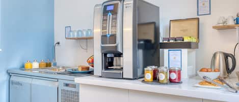 A commercial kitchen with a coffee machine, a refrigerator, and various food items on the counter.