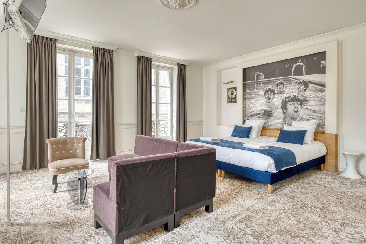 A hotel room with a bed, a chair, a small table, and a large window with curtains.