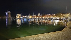 A nighttime marina with boats docked along the waterfront, a prominent tower, and buildings with lights. - Hotel François 1er Cœur de Ville (La Rochelle)