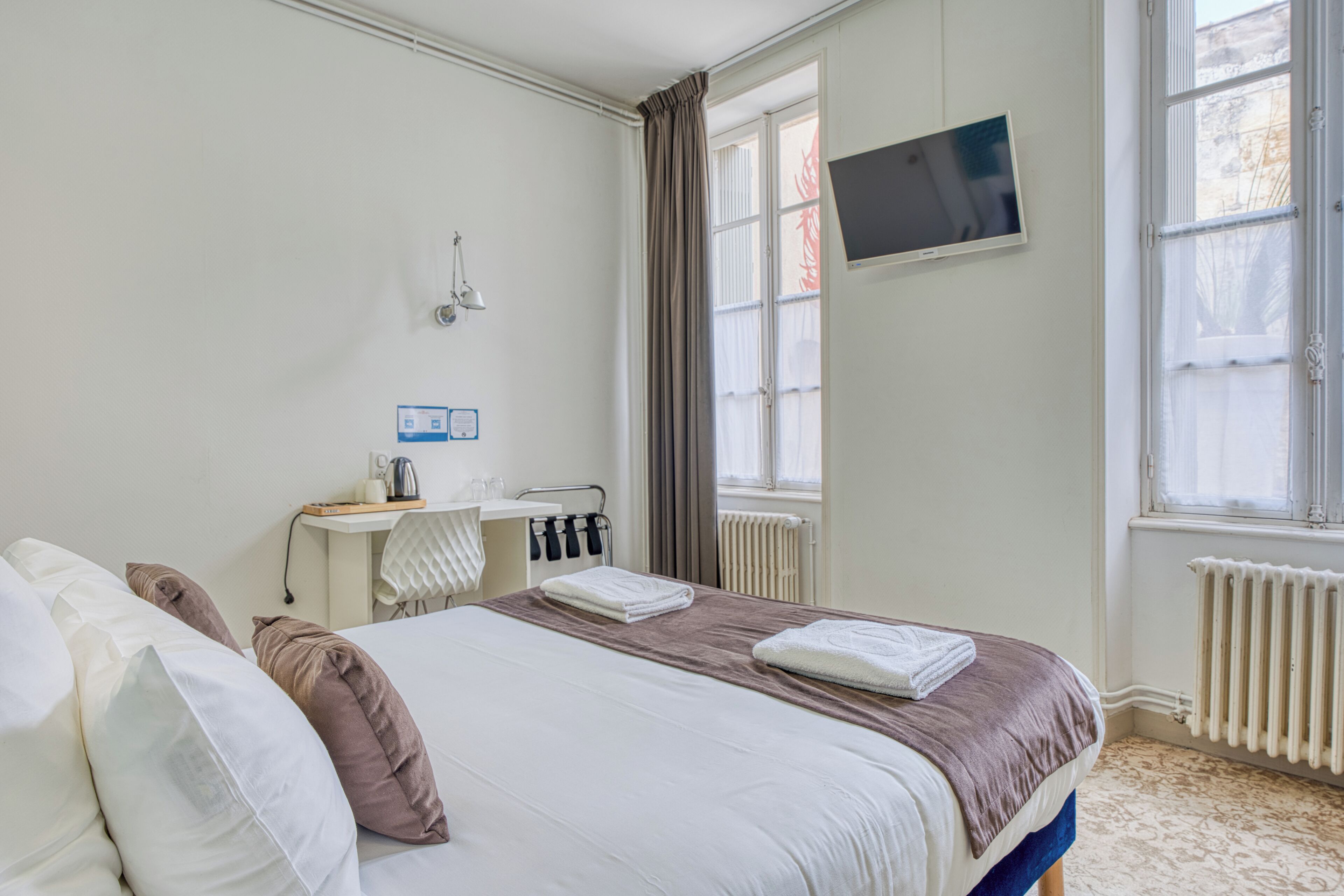 Et hotelværelse med seng, fjernsyn ophængt på væggen, et vindue med gardiner og en radiator.