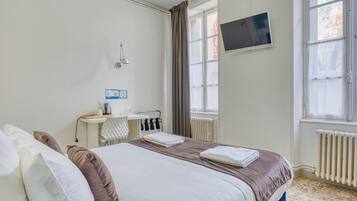Una habitación de hotel con cama, televisor montado en la pared, ventana con cortinas y radiador.