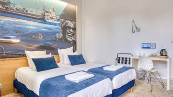 Ein Hotelzimmer mit zwei Betten, einem Schreibtisch, einem Stuhl und einem großen Gemälde eines Schiffes an der Wand.