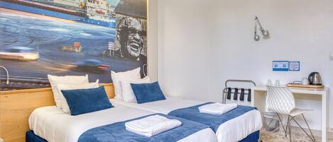 A hotel room with two beds, a desk, a chair, and a large painting of a ship on the wall.