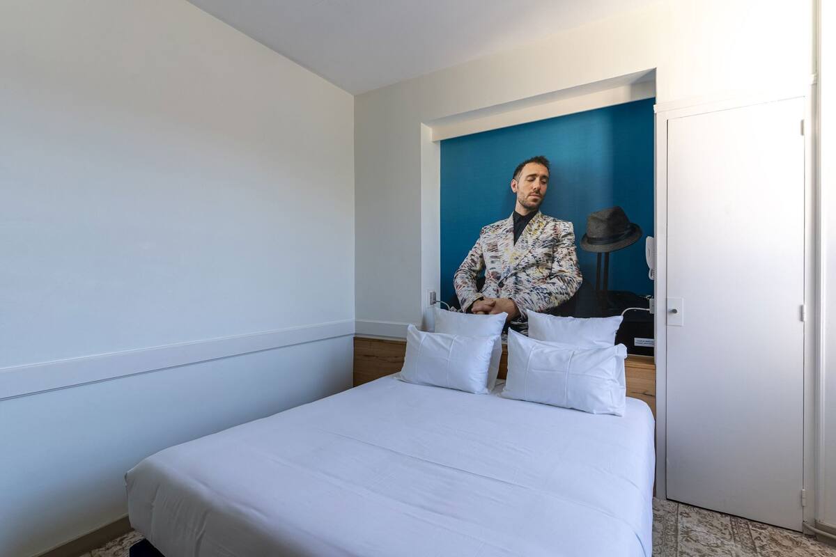 A hotel room with a bed, a blue accent wall, and a portrait of a man in a suit.