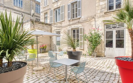 An outdoor patio with a table and chairs, surrounded by potted plants and a cobblestone floor.