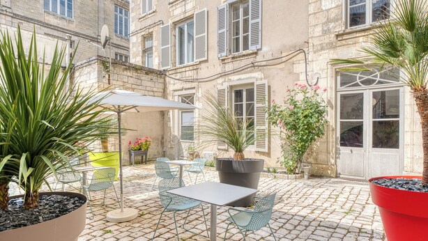 An outdoor patio with a table and chairs, surrounded by potted plants and a cobblestone floor. - Hotel François 1er Cœur de Ville (La Rochelle)