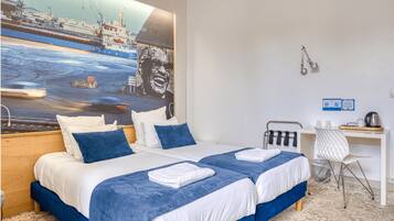 Une chambre d’hôtel avec deux lits, un bureau, une chaise et un grand tableau représentant un navire accroché au mur.