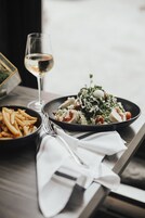 Una mesa con un plato de comida, una copa de vino blanco y un tenedor.