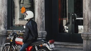 Una persona sentada en una motocicleta frente a un edificio con grandes columnas y una puerta con el número 168.