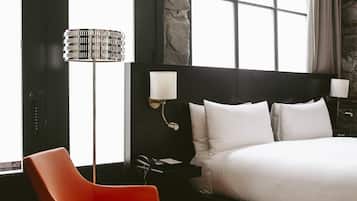 Ett modernt hotellrum med en stor säng, en röd fåtölj, en golvlampa och en vägg som har en dekorativ stenbeklädnad.
