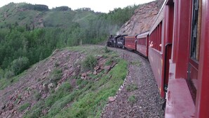 A train moving along a track through a mountainous area with dense forests. - Narrow Gauge Railroad Inn (Antonito)