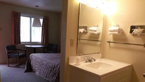A hotel room with a bed, a round table, two chairs, a bathroom with a sink and mirror, and towels on the wall. - Narrow Gauge Railroad Inn (Antonito)