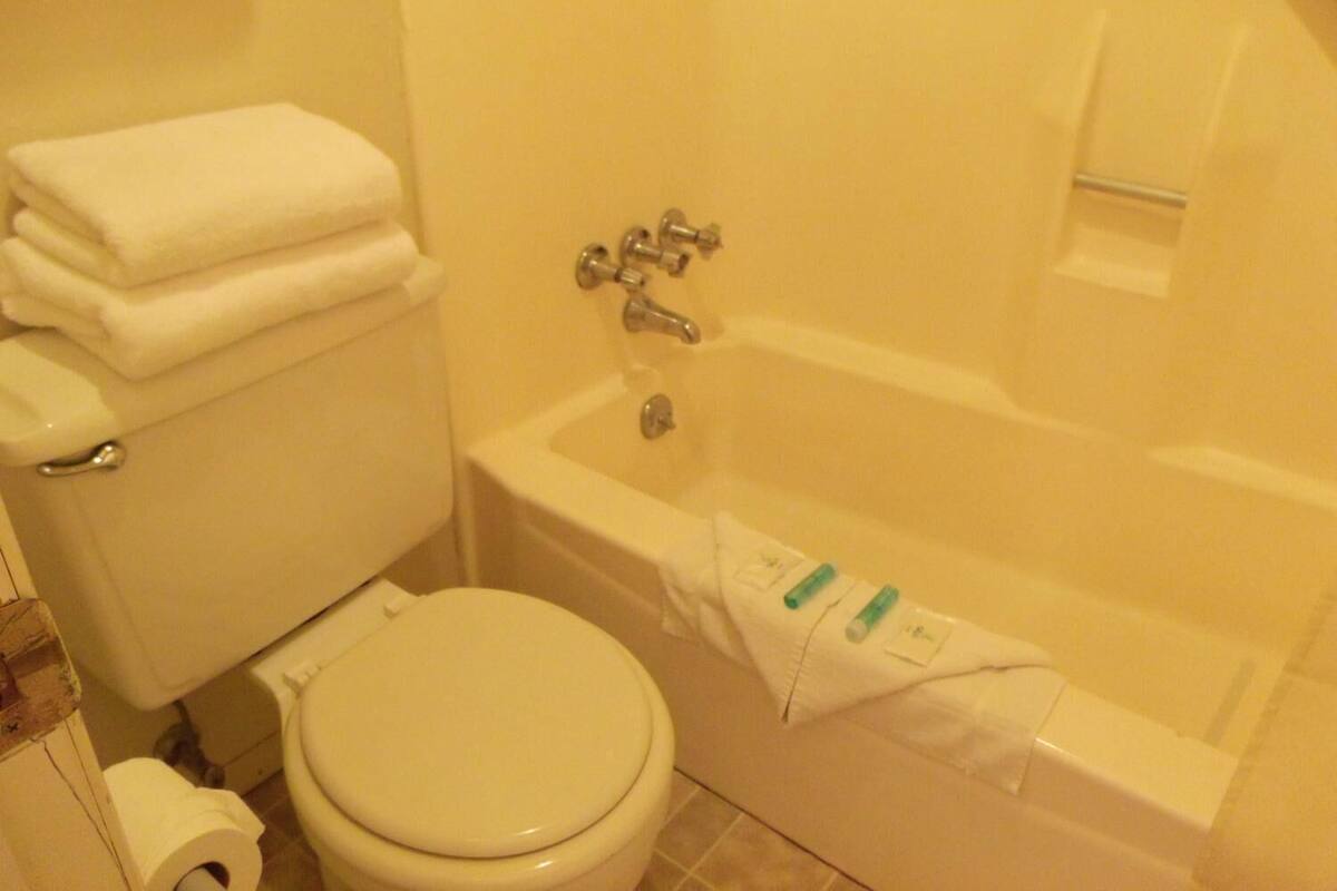 A bathroom with a toilet, a stack of white towels, and a bathtub.