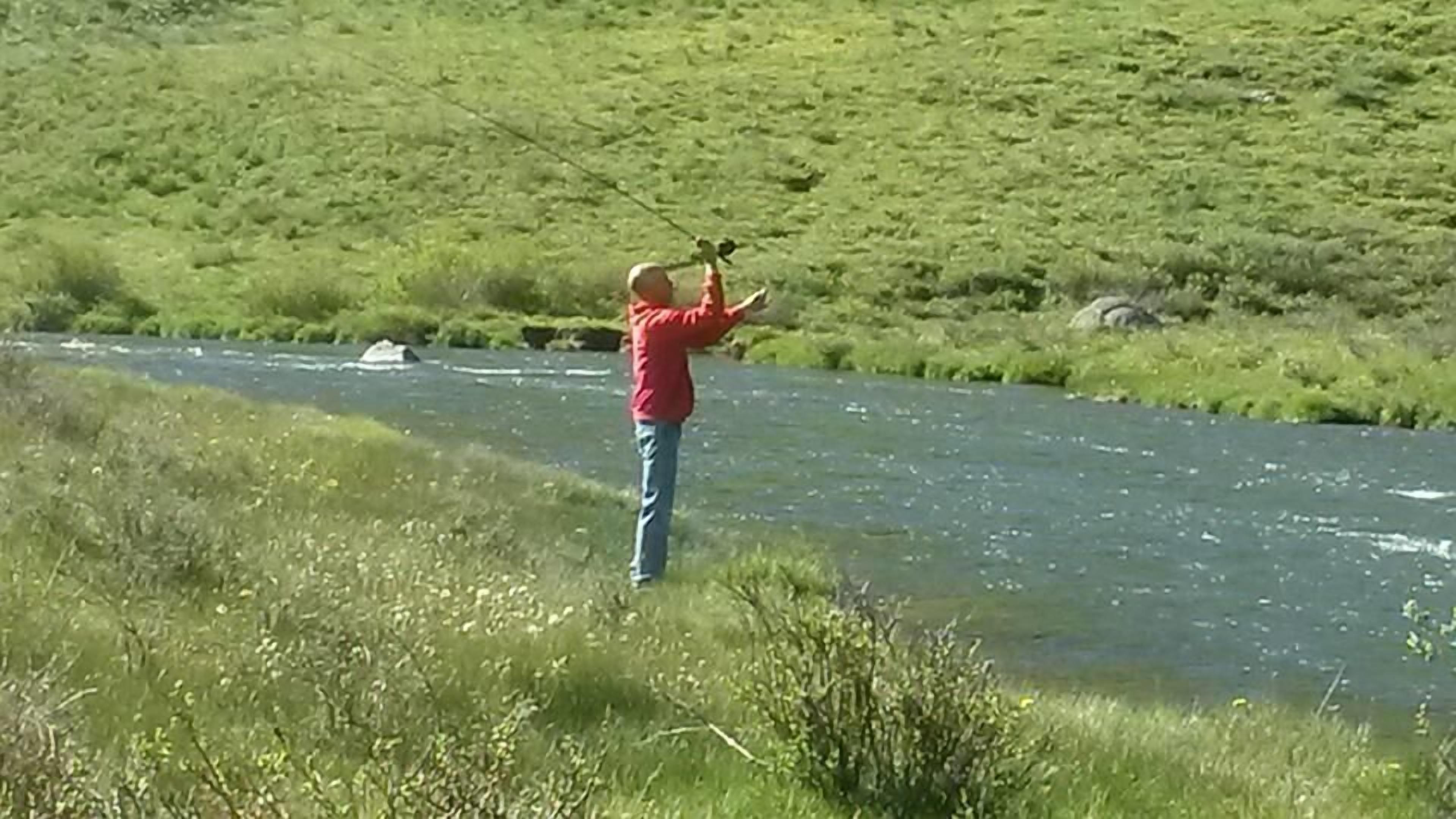 A person standing by a river, holding a camera.
