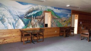 A dining area with wooden tables and chairs, a mural depicting a mountainous landscape with a train, and a wooden interior. - Narrow Gauge Railroad Inn (Antonito)