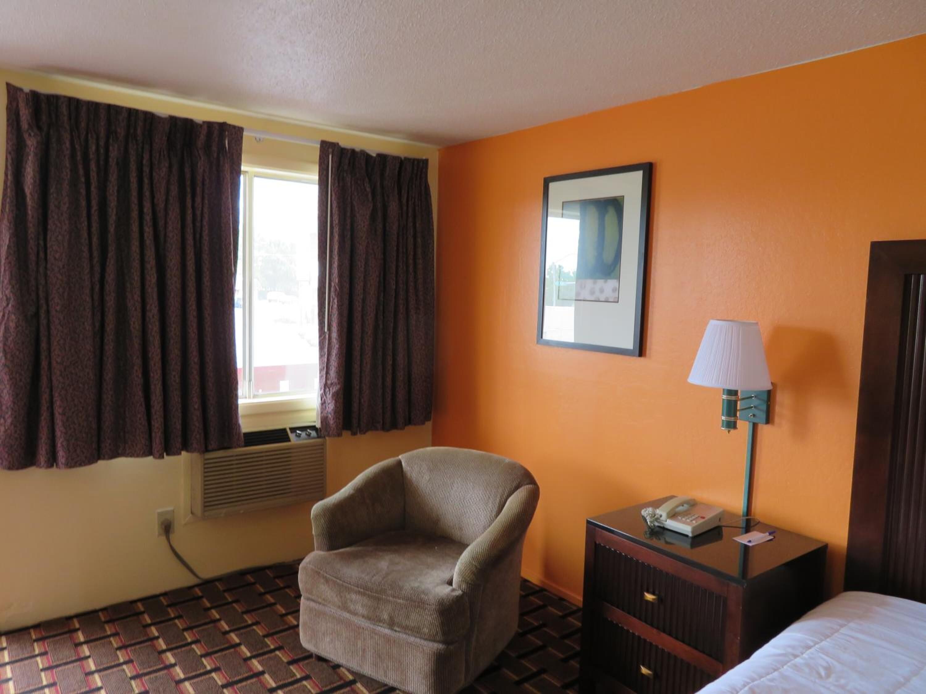 A hotel room with a patterned floor, a chair, a bedside table with a lamp, and a bed.