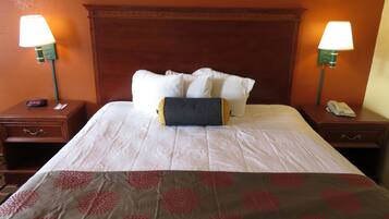 A hotel room with a neatly made bed, two bedside tables with lamps, a clock, and a phone on one of the tables.