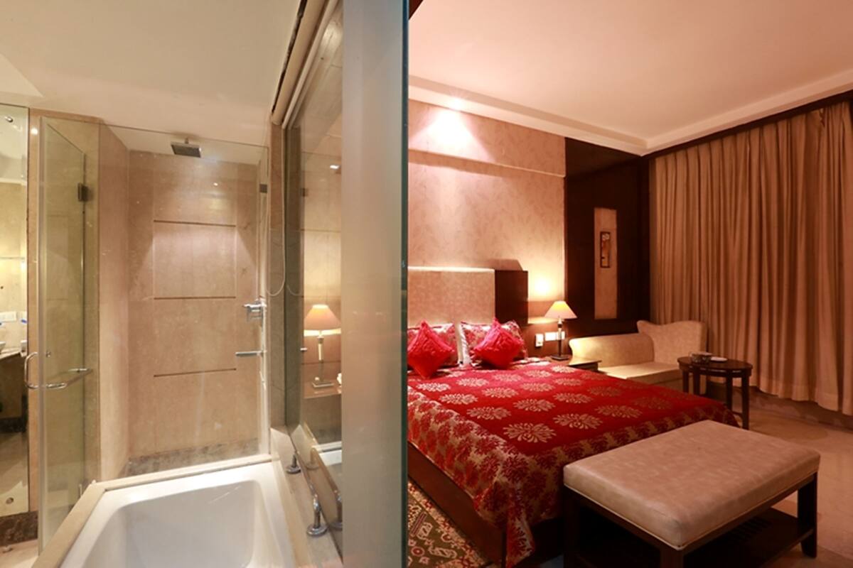 Une chambre d’hôtel avec une douche en verre, un grand lit avec une literie rouge, une table de chevet et une chaise.