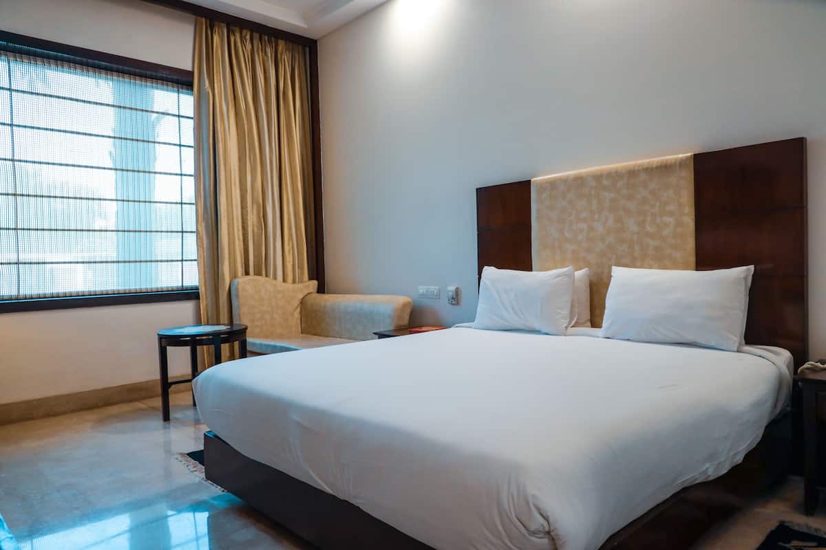 Une chambre d’hôtel avec un grand lit, une petite table de chevet, une chaise, une fenêtre avec des rideaux et un téléphone fixé au mur.