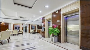 Een hotel lobby met een receptiebalie, een zithoek en een lift.