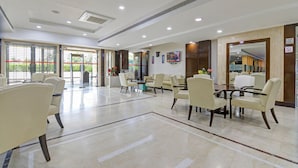 Een ruime lobby met een hoge plafond, ingebouwde verlichting, en een zithoek met stoelen en tafels.