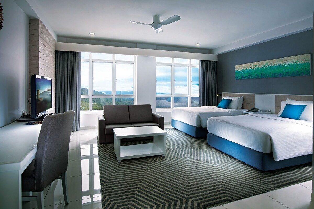 A modern hotel room with a large window, a flat-screen TV, a sofa, two beds, and a ceiling fan.
