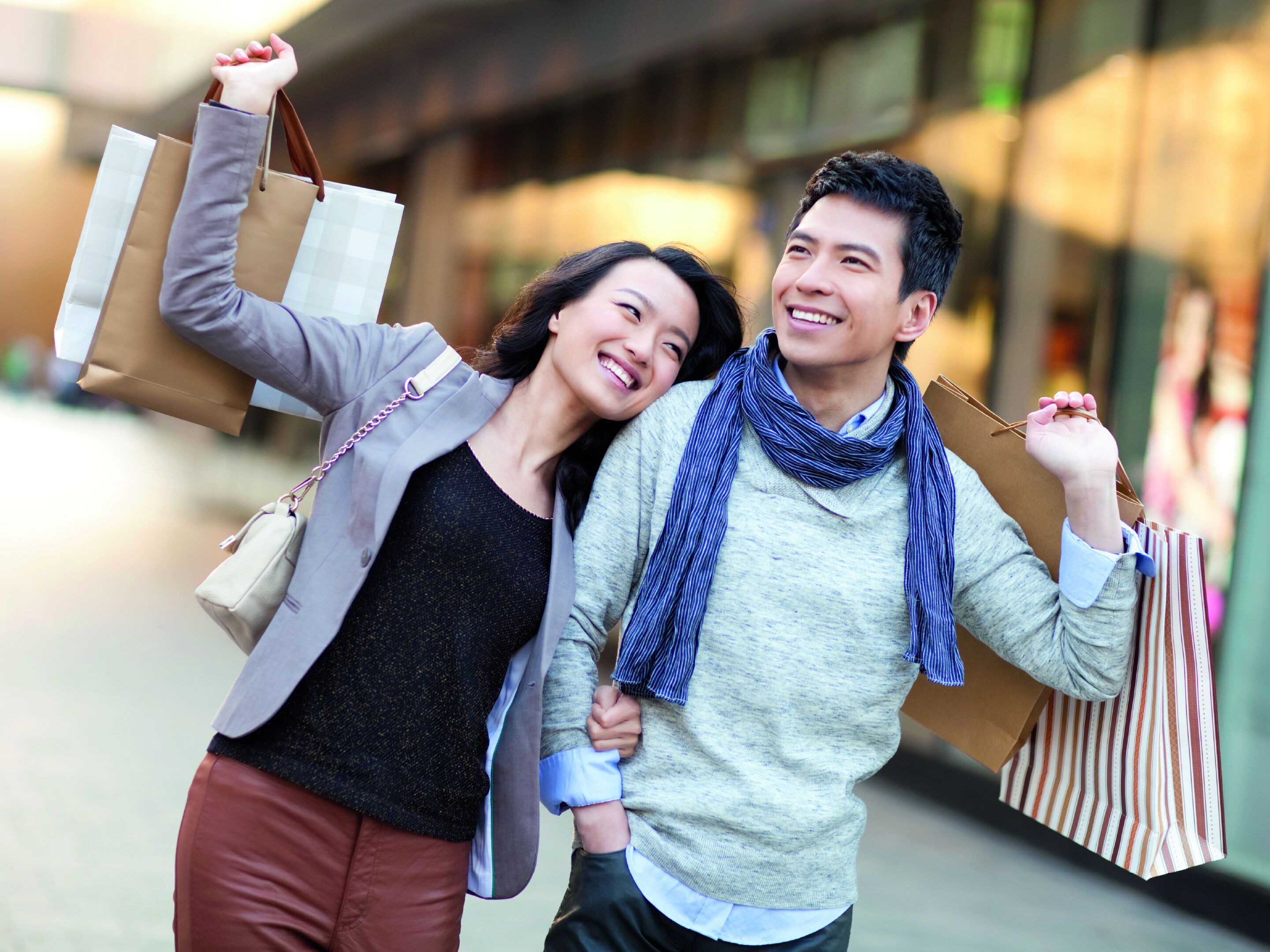 A couple holding shopping bags, walking outdoors.