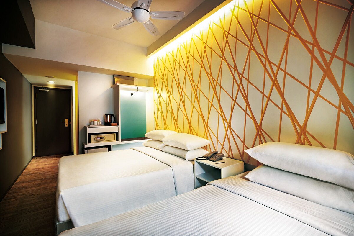 A hotel room with two beds, a desk, a chair, a wardrobe, and a ceiling fan.