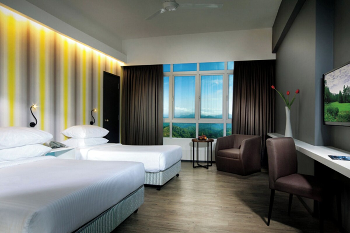 A modern hotel room with two beds, a desk, a chair, and a view of a green landscape through large windows.
