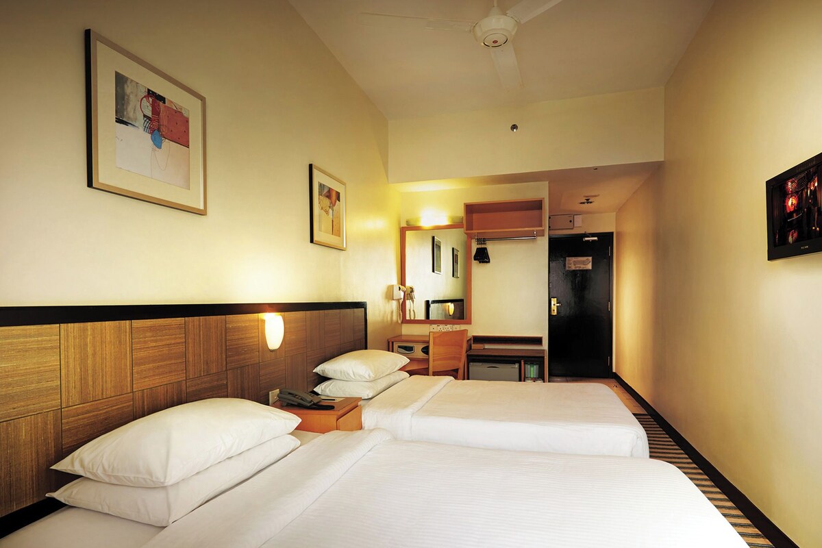 A hotel room with two beds, a desk, a chair, a mirror, and a door.
