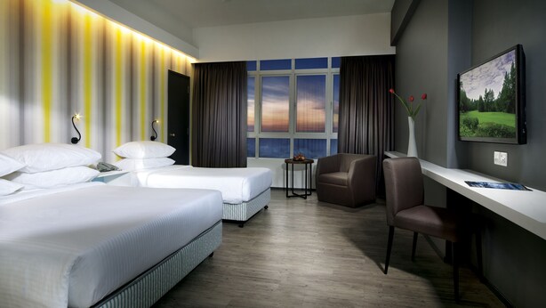 A hotel room with two beds, a desk, a chair, a TV, a ceiling fan, and a view of the sunset through the window. - Resorts World Genting - First World Hotel (Genting Highlands)