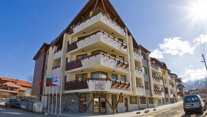 Un hotel de varios pisos con balcones, un letrero que indica que es un complejo turístico de montaña, y un cielo despejado.