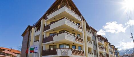 A multi-story hotel with balconies, a sign indicating it is a mountain resort, and a clear sky.