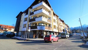 Un hotel de varios pisos con balcones, un estacionamiento y el paisaje de montañas al fondo.