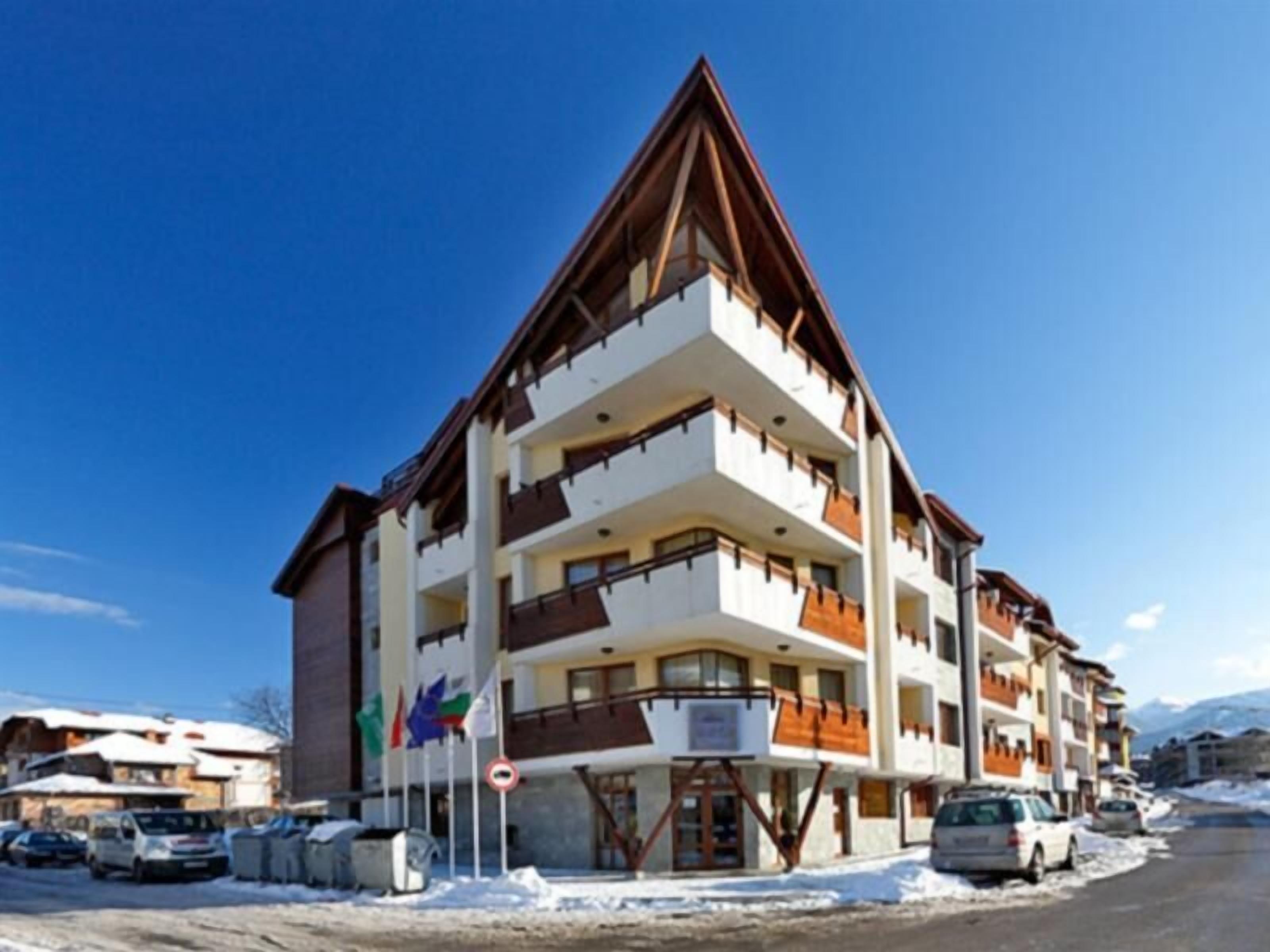 A multi-story hotel with balconies, a ski lift, and a parking area with cars.