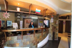 A reception area with a stone counter, a flag, and a computer monitor. - Mountview Lodge (Bansko)