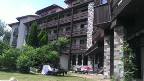 A multi-story building with balconies, a covered outdoor seating area, and lush greenery. - Hotel Orphey Bansko (Bansko)