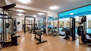 A gym with various exercise equipment, a bench, and a large window with a view of a swimming pool. - Hotel Orphey Bansko (Bansko)