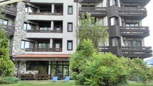 A multi-story building with balconies, a covered outdoor seating area, and a well-maintained garden. - Hotel Orphey Bansko (Bansko)