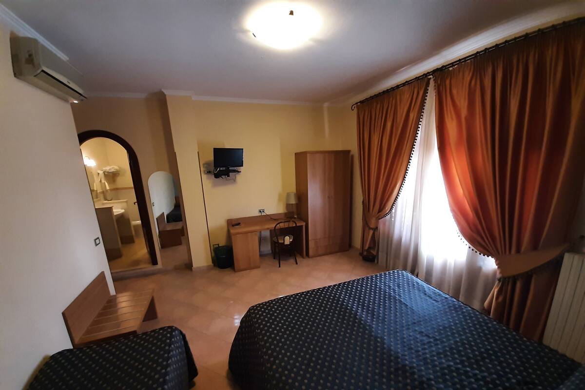 A hotel room with two beds, a desk, a chair, a television, and a wardrobe.
