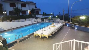 Ein Essbereich am Pool mit einem langen Tisch, gedeckt für eine Mahlzeit, umgeben von Stühlen.