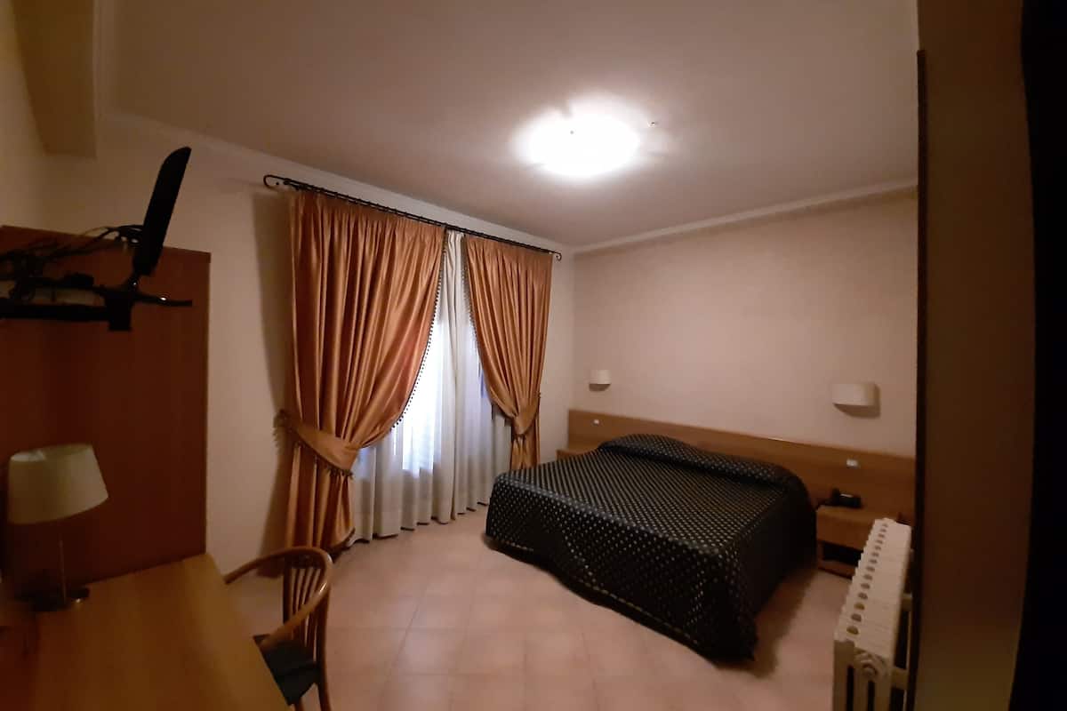 A hotel room with a bed, a chair, a desk with a lamp, and curtains.