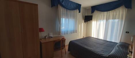 A bedroom with a bed, a desk, a wardrobe, and a television.