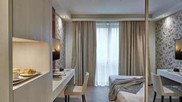 Une chambre d’hôtel équipée d’un lit, d’un bureau, d’une chaise, d’une télévision et d’une grande fenêtre avec des rideaux.
